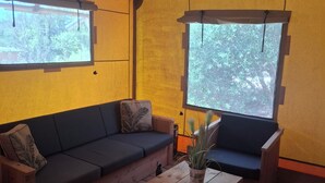 Una habitación con piso de madera, un sofá, una mesa de centro y dos ventanas con cortinas.