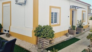 Ein weißes Gebäude mit gelben Verzierungen, einer geschlossenen Rolltür und einem kleinen Gartenbereich mit Topfpflanzen.