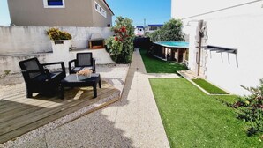 Ein Wohnhaus mit einer Terrassenfläche, Gartenmöbeln im Freien, einem kleinen Pool und einem gepflegten Rasen.