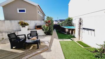 Ein Wohnhaus mit einer Terrassenfläche, Gartenmöbeln im Freien, einem kleinen Pool und einem gepflegten Rasen.