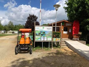 Entorno rural con un edificio de madera identificado con la señal 'Accueil' y un cartel con diversa información.