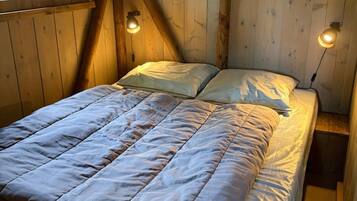 A wooden room with a bed, two wall-mounted lamps, and a window.