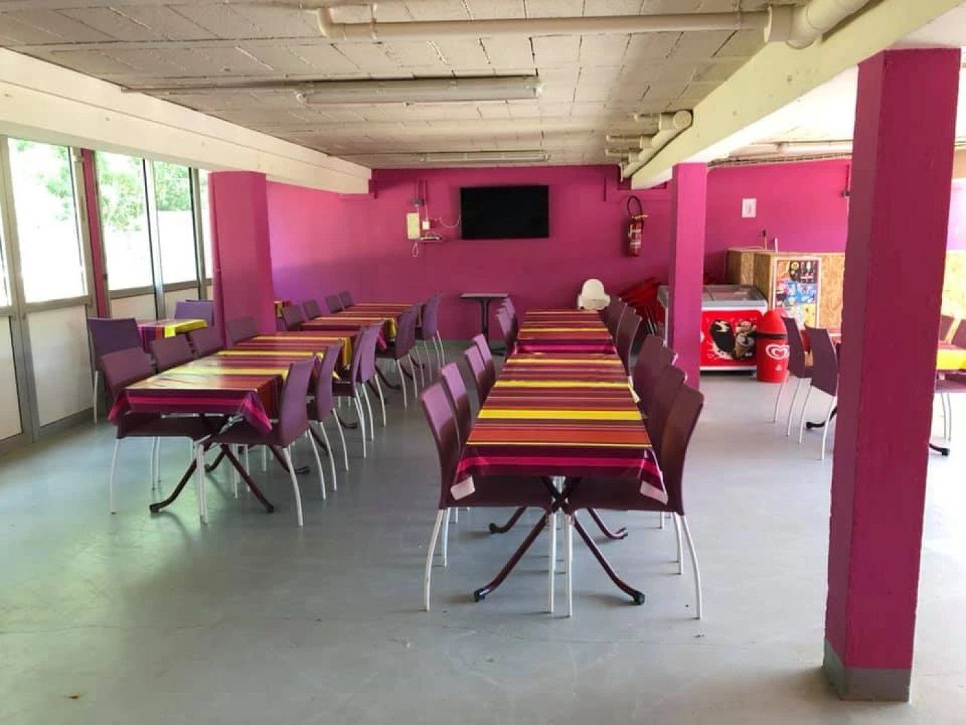 A conference room with multiple tables and chairs, a flat-screen TV mounted on the wall, and a vending machine in the corner.