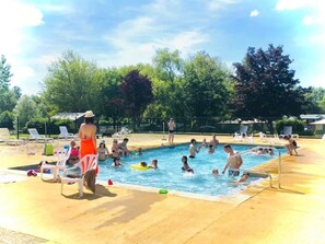 Una piscina rodeada de sillas de descanso y sombrillas, con gente nadando y relajándose.