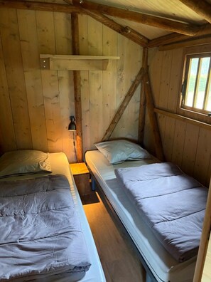 A cabin-style room with two single beds, a wooden ceiling, and a window.