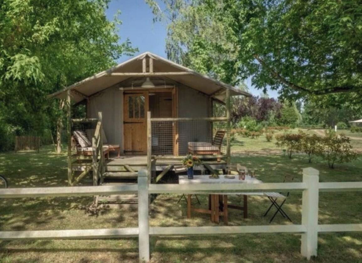 Een klein houten vakantiehuisje met een veranda, omringd door een witte hek en bomen.