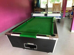 A pool table with a green felt surface, a white and black table frame, and a visible logo on the side.