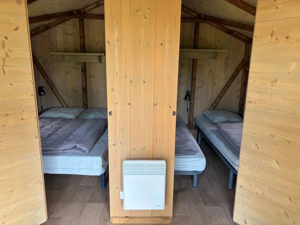 Een klein houten huisje met twee bedden, elk voorzien van een matras en kussens.