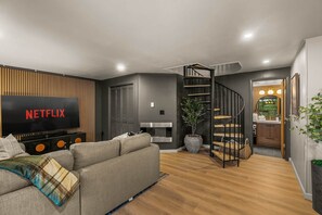 Ein modernes Wohnzimmer mit Flachbildfernseher, einer Treppe und einer Küchenzeile.