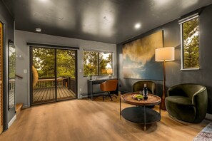 Ein modernes Interieur mit Holzboden, Schreibtisch, Stuhl, rundem Tisch mit einer Flasche und Obst, sowie einem Gemälde an der Wand.