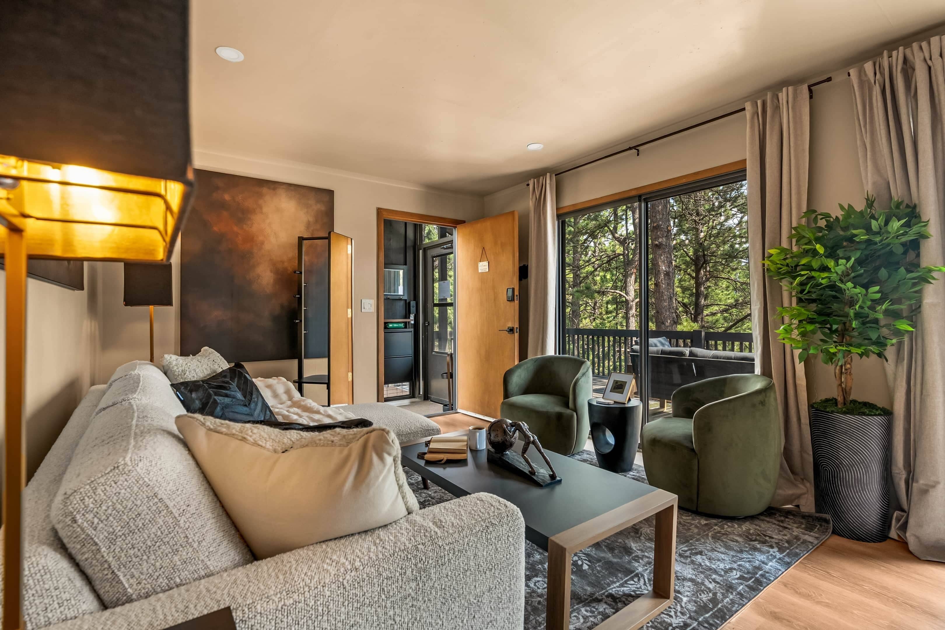 A modern living room with a sofa, armchairs, a coffee table, and a large window with a view of trees.