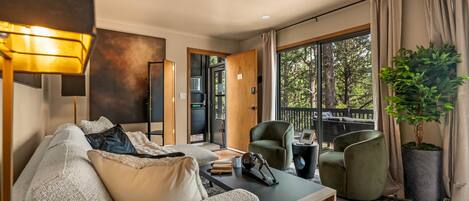 A modern living room with a sofa, armchairs, a coffee table, and a large window with a view of trees.