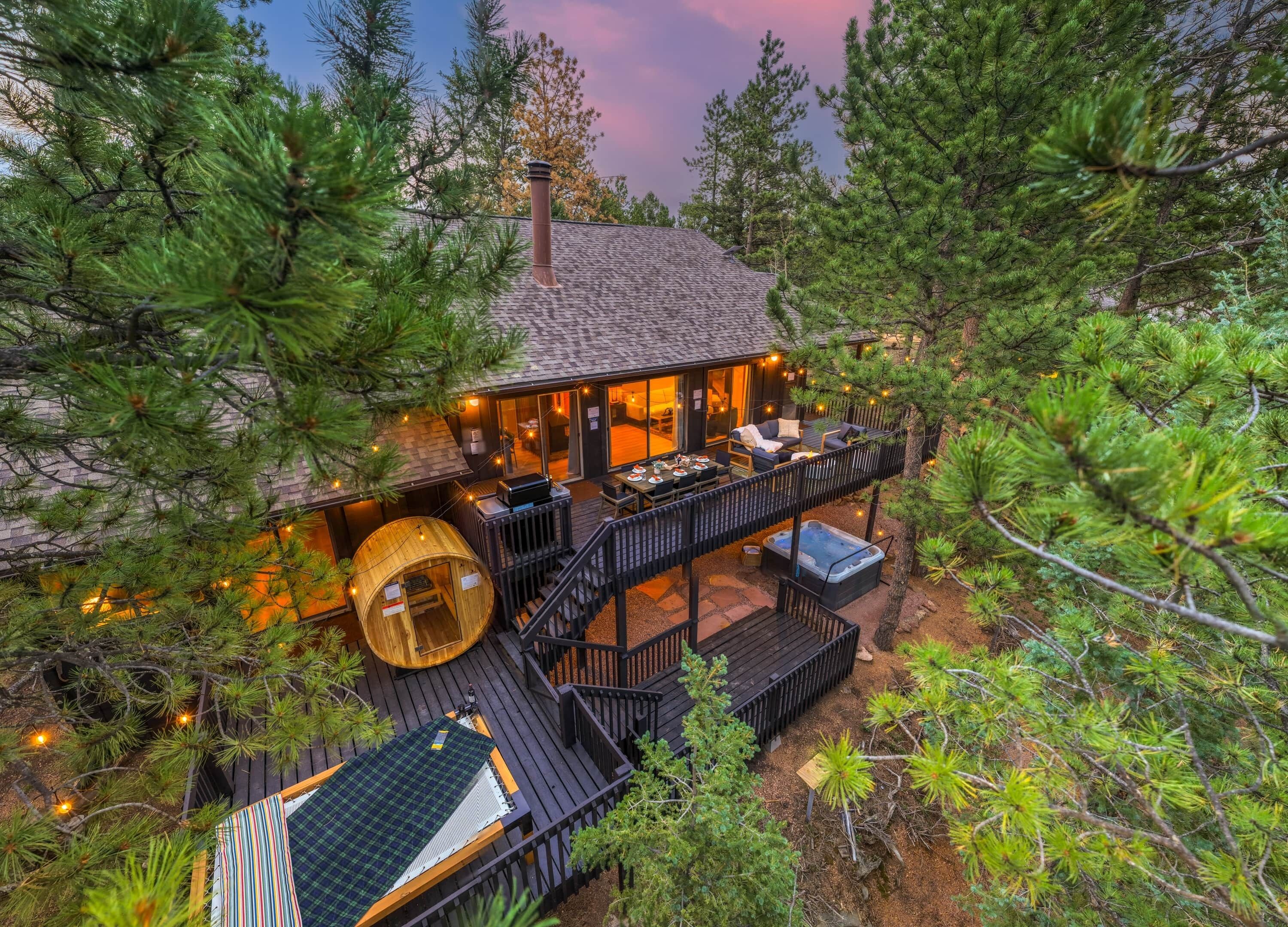 A cabin with a deck, hot tub, and outdoor seating area surrounded by trees.