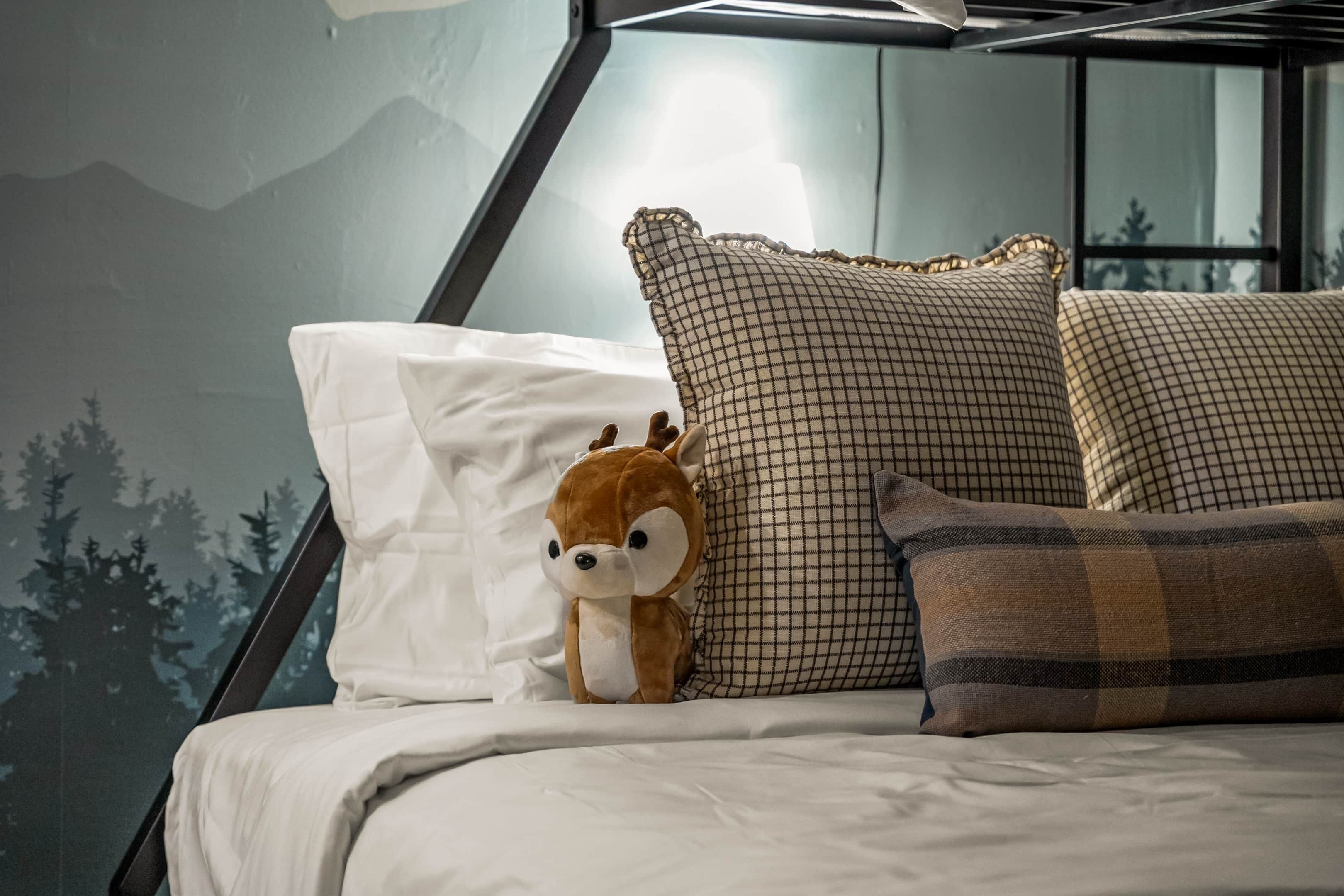 A bed with a white pillow, a brown plush toy, and two patterned pillows.