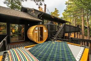 Eine Holz-Sauna mit Glastür, eine Holzterrasse mit karierter Matte und eine Treppe zu einer erhöhten Ebene.