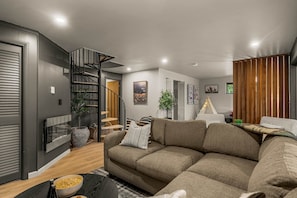Een moderne woonkamer met een hoekbank, een open haard, een trap en een eethoek.