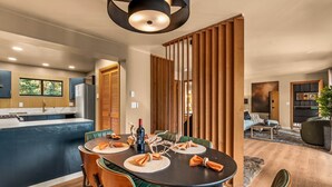Uma cozinha moderna com geladeira embutida, um espaço de refeições com mesa redonda e cadeiras, e uma sala de estar com sofá e mesa de centro.