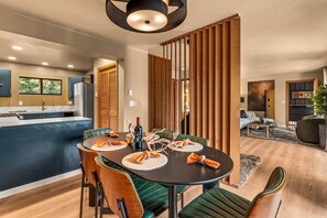 Eine moderne Küche mit Einbaukühlschrank, ein Essbereich mit rundem Tisch und Stühlen sowie ein Wohnzimmer mit Sofa und Couchtisch.