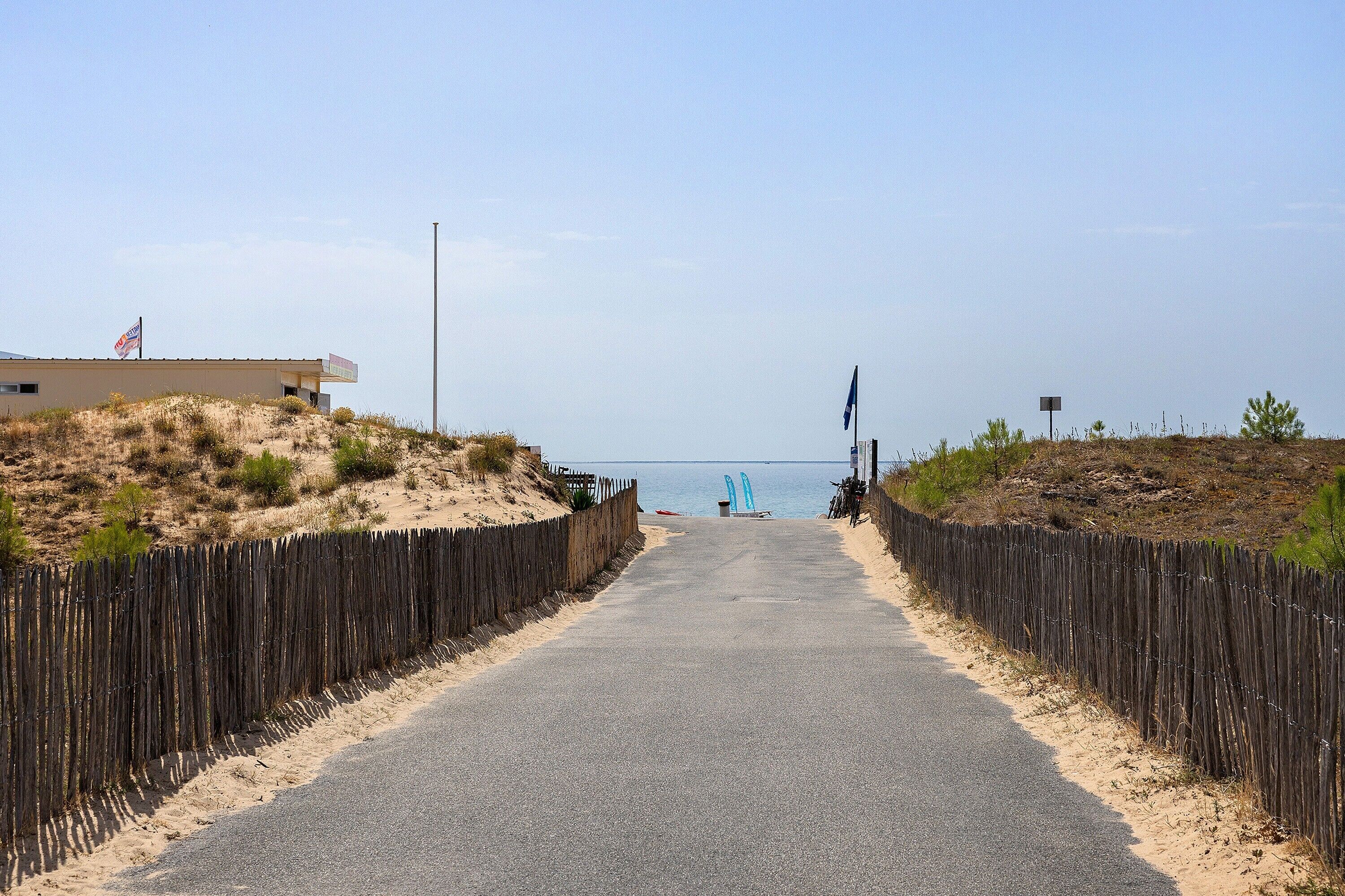 A paved pathway leading to a beach with a wooden fence on either side.