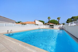 A rectangular swimming pool with clear blue water, surrounded by a white wall and a white fence.