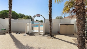 A gated entrance with a sign indicating a time limit, a pool area with a fence, and palm trees.