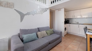 A modern interior with a grey sofa, a wall-mounted fish sculpture, and a kitchen area.