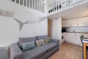 A modern interior with a grey sofa, a wall-mounted fish sculpture, and a kitchen area.