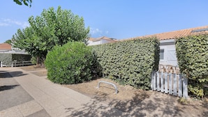 A residential area with a paved driveway, a white fence, and a well-maintained hedge.