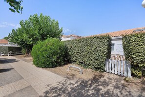 A residential area with a paved driveway, a white fence, and a well-maintained hedge.