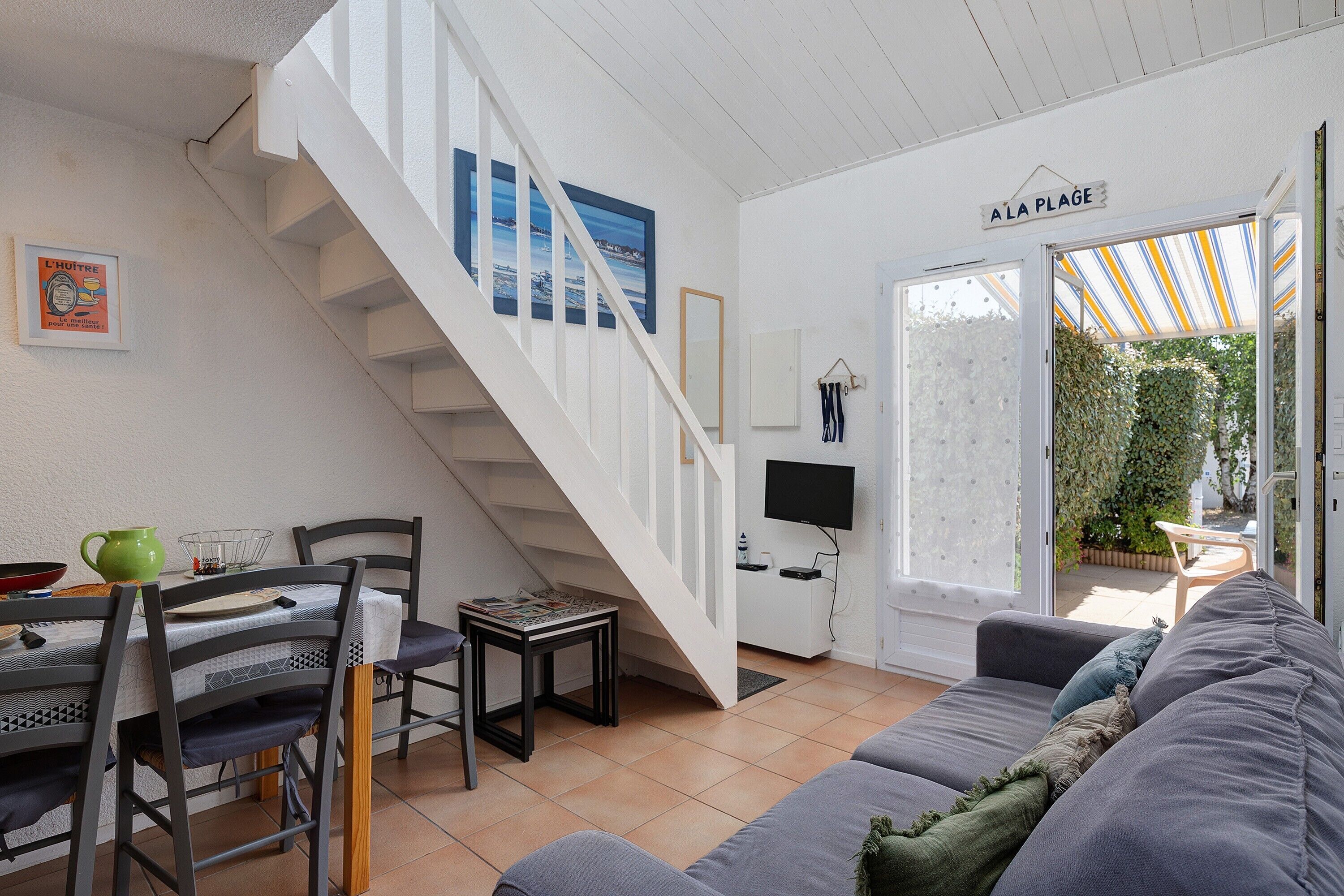 Una sala de estar con escalera, comedor y televisor en la pared.