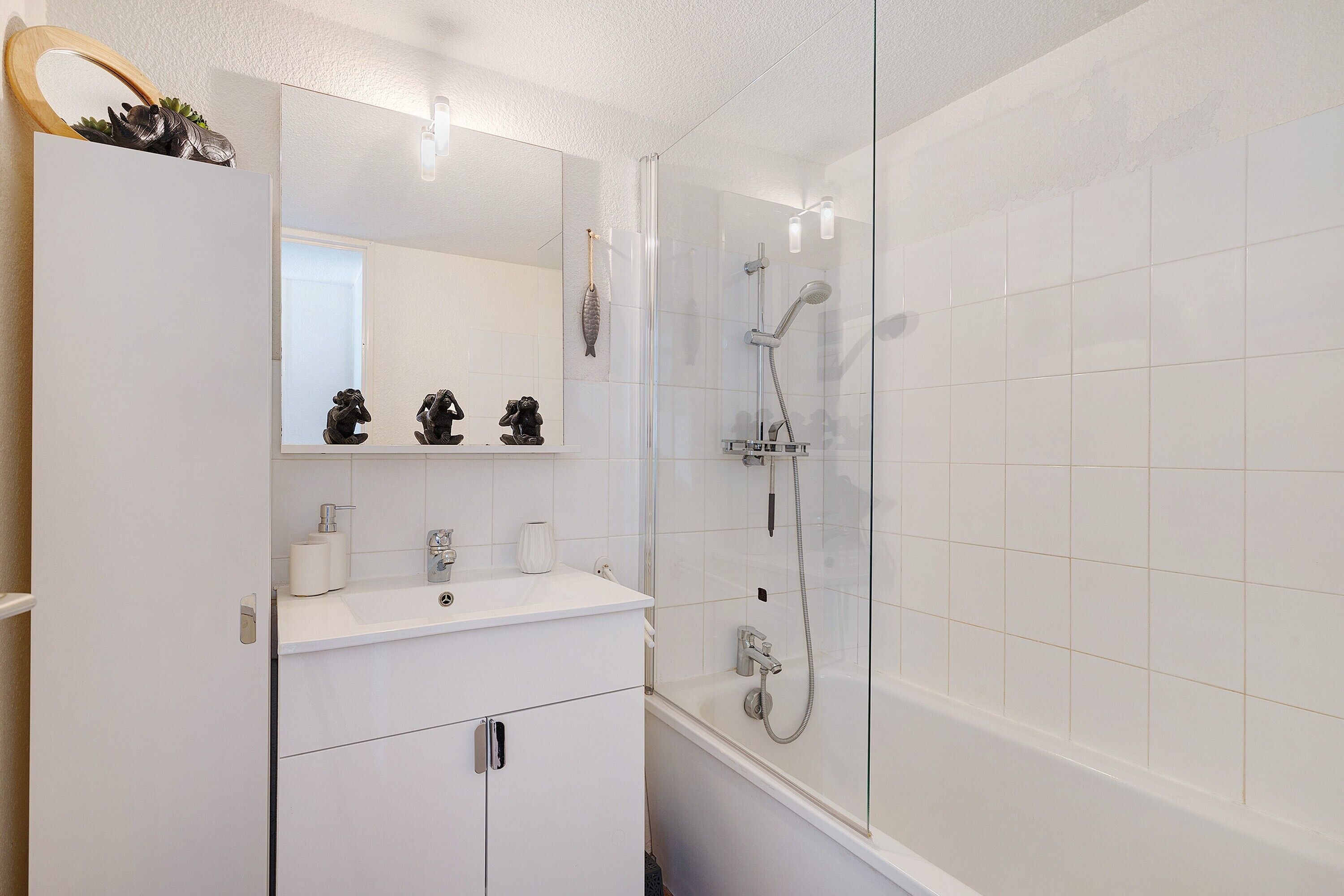 Un baño con lavamanos, espejo y ducha blancos.