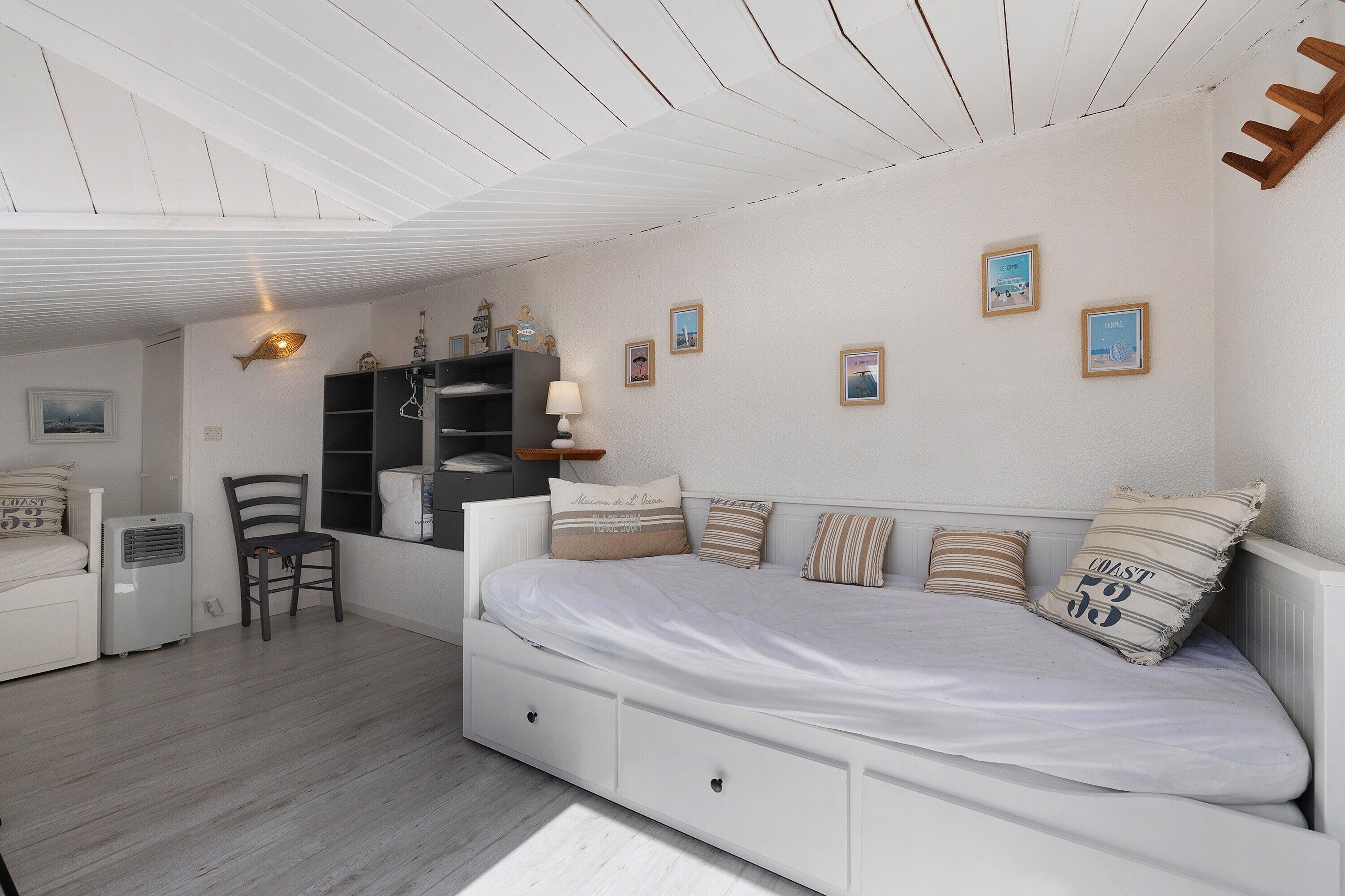 Een slaapkamer met een bed, een stoel, een nachtkastje, een lamp en een plank met decoratieve objecten.