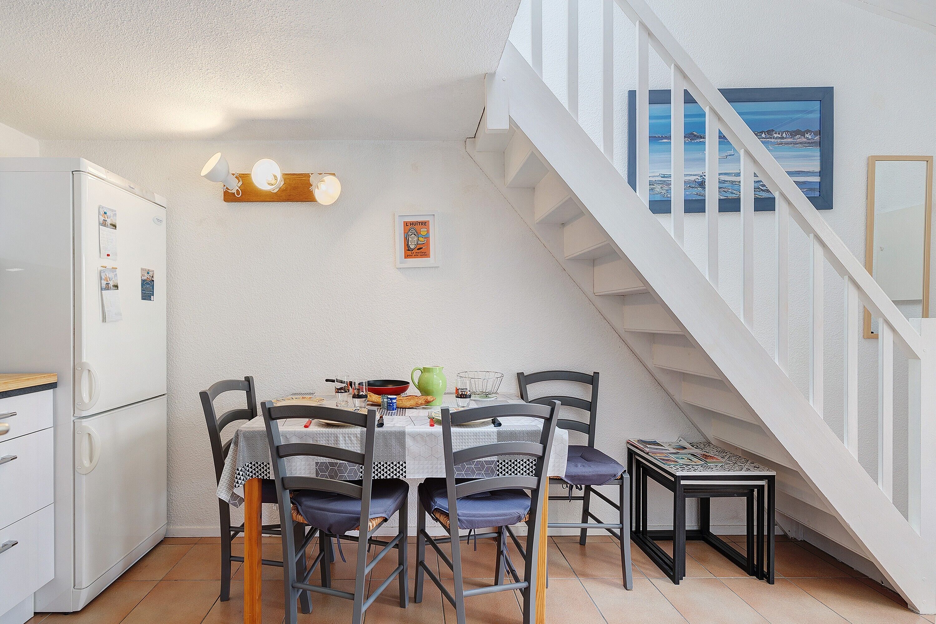 Une cuisine compacte comprenant une table à manger pour quatre personnes, un réfrigérateur et un escalier menant à l’étage supérieur.