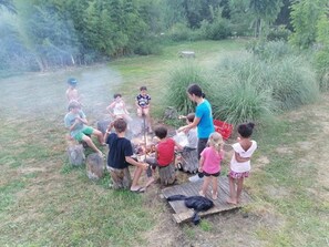 A group of people gathered around a campfire in an outdoor setting with trees and grass.