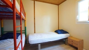 A single bed with a wooden frame, a small bedside table, and a window with curtains.