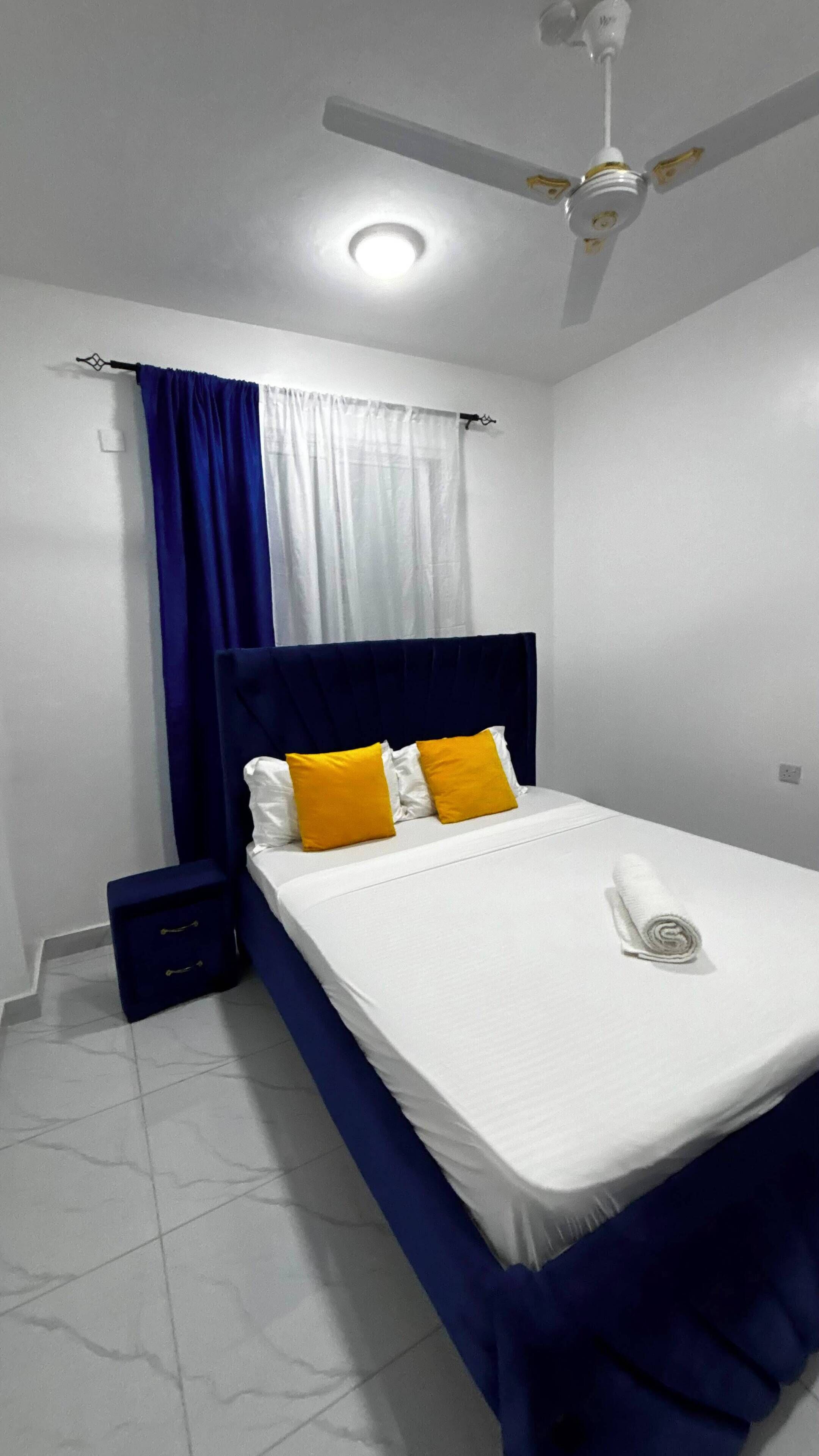 Un dormitorio con cama, cortinas, mesita de noche y ventilador de techo.