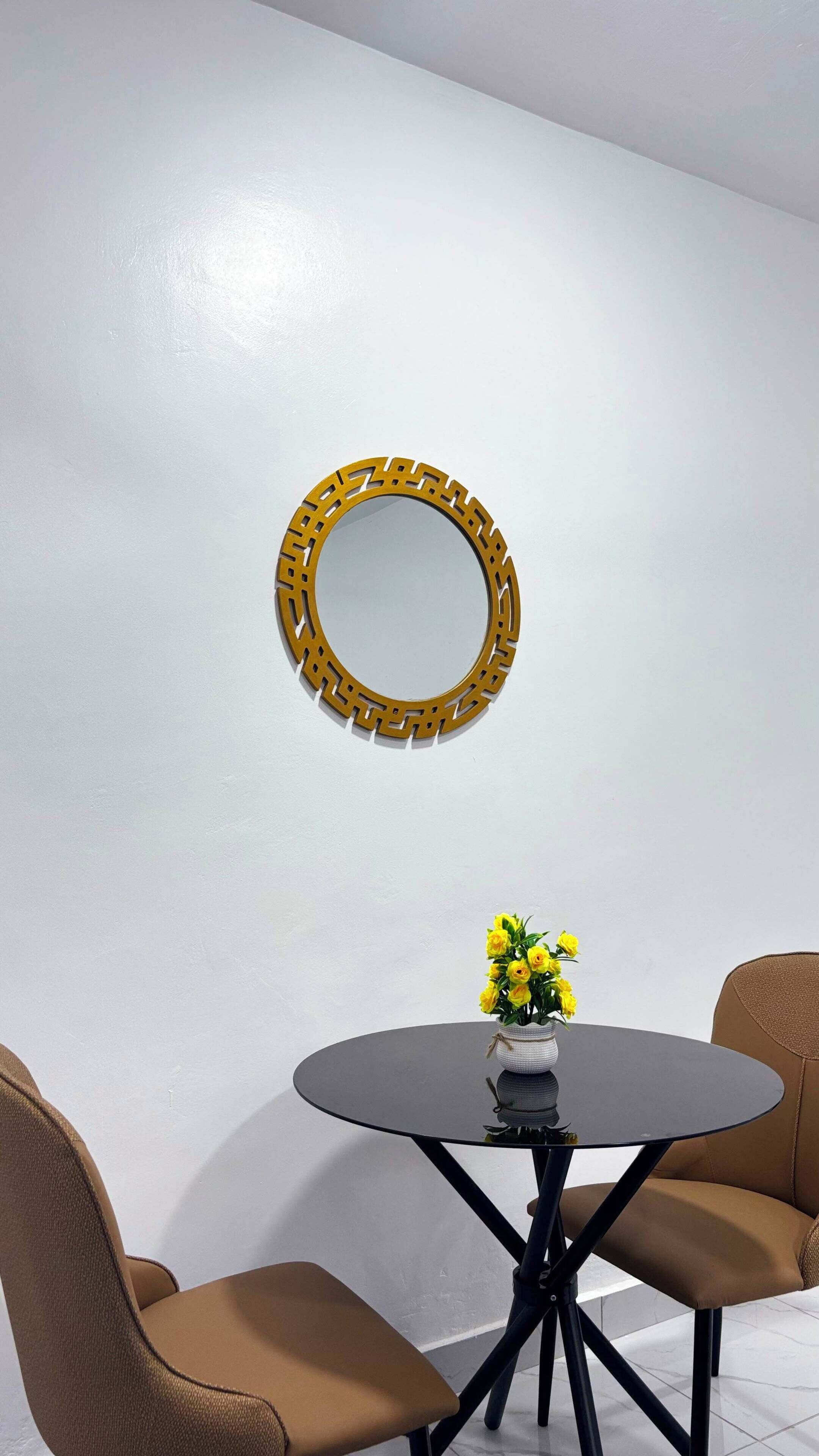 A round table with a vase of yellow flowers, two chairs, and a decorative wall piece.