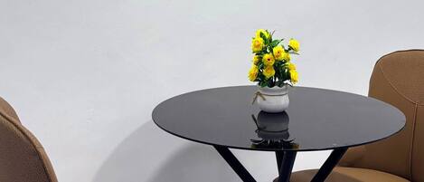 Une table ronde ornée d’un vase de fleurs jaunes, deux chaises et un élément décoratif mural.