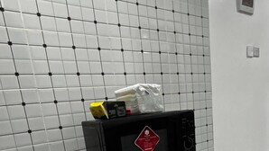 Un área de cocina con un microondas sobre un pedestal, un refrigerador pequeño y un salpicadero de azulejos.