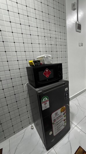 Eine Küchenzeile mit einer auf einem Stand gebauten Mikrowelle, einem kleinen Kühlschrank und einer gefliesten Rückwand.