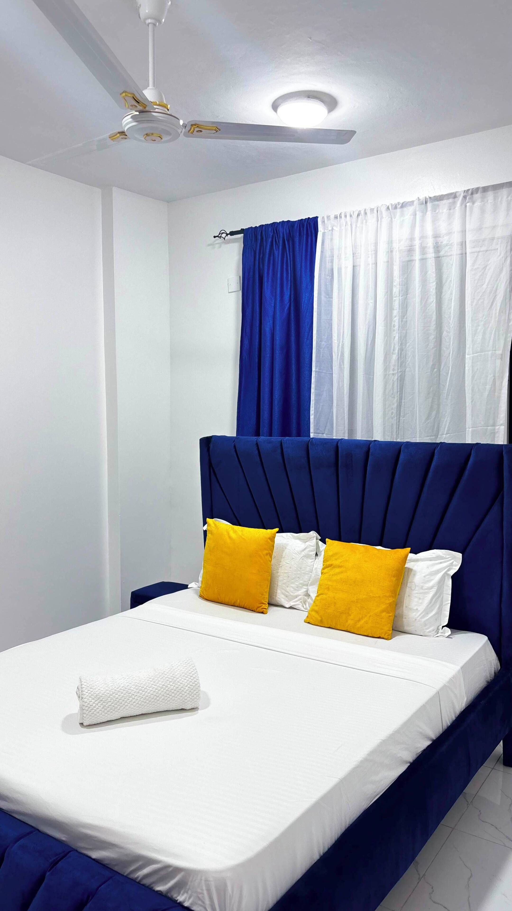 A bedroom with a bed, a ceiling fan, and curtains.