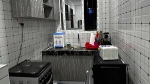 Una cocina compacta con paredes de azulejos blancos, estufa integrada, un lavamanos y una ventana.