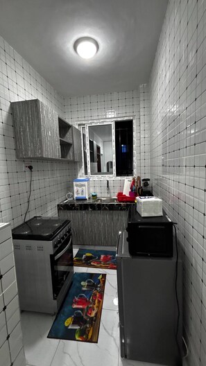 Eine kleine Küche mit weiß gefliesten Wänden, einem Einbauherd, einer Spüle und einem Fenster.