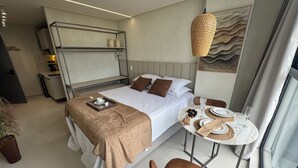 A modern hotel room with a bed, bedside table, and a dining area with a table and chairs. - Breeze Studio Vista Mar Jardim Oceania (João Pessoa)
