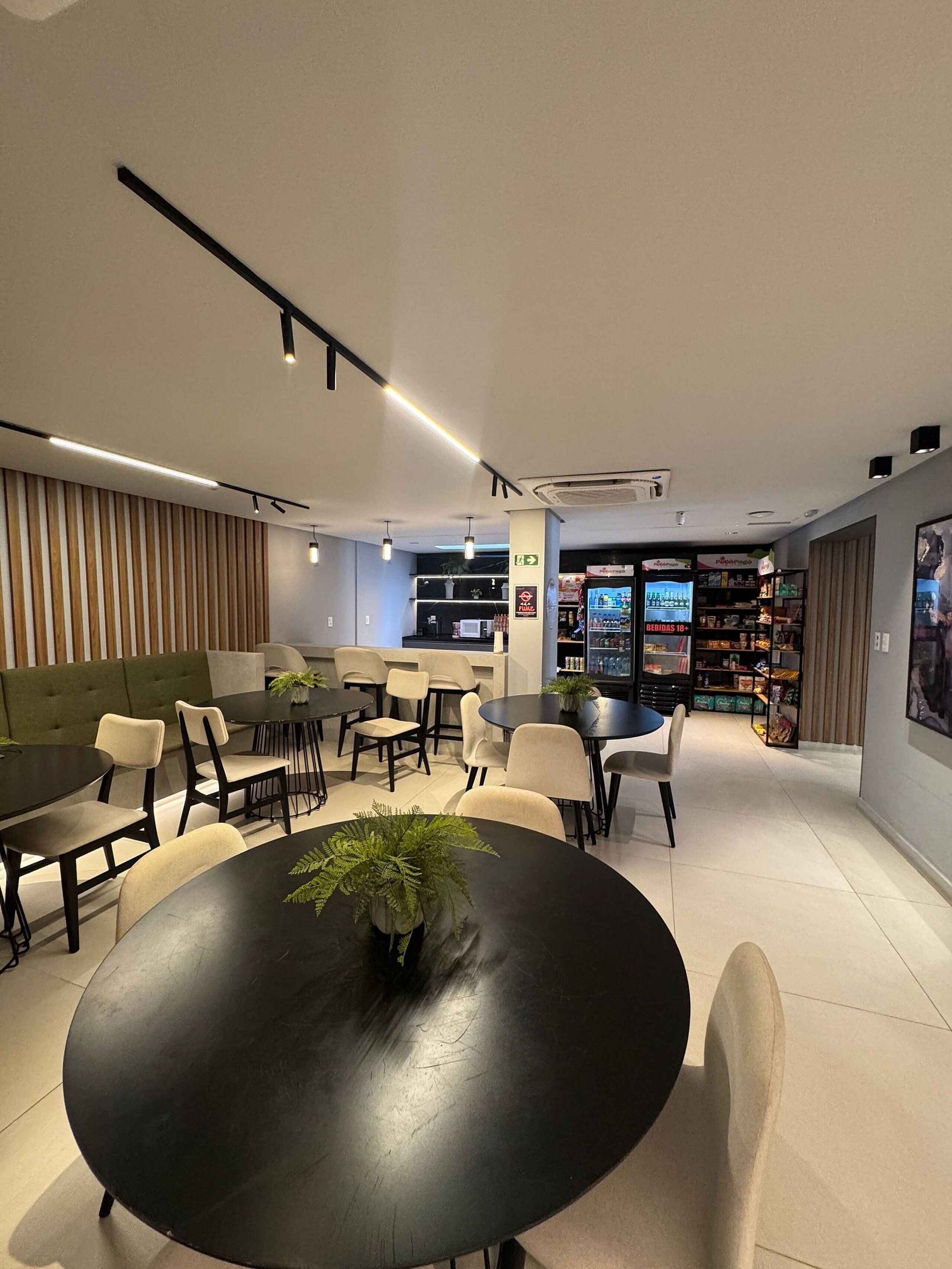 Um interior moderno com uma mesa redonda em primeiro plano, um sofá verde e um espaço de bar ao fundo.