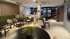 A modern interior with a round table in the foreground, a green sofa, and a bar area in the background. - Breeze Studio Vista Mar Jardim Oceania (João Pessoa)