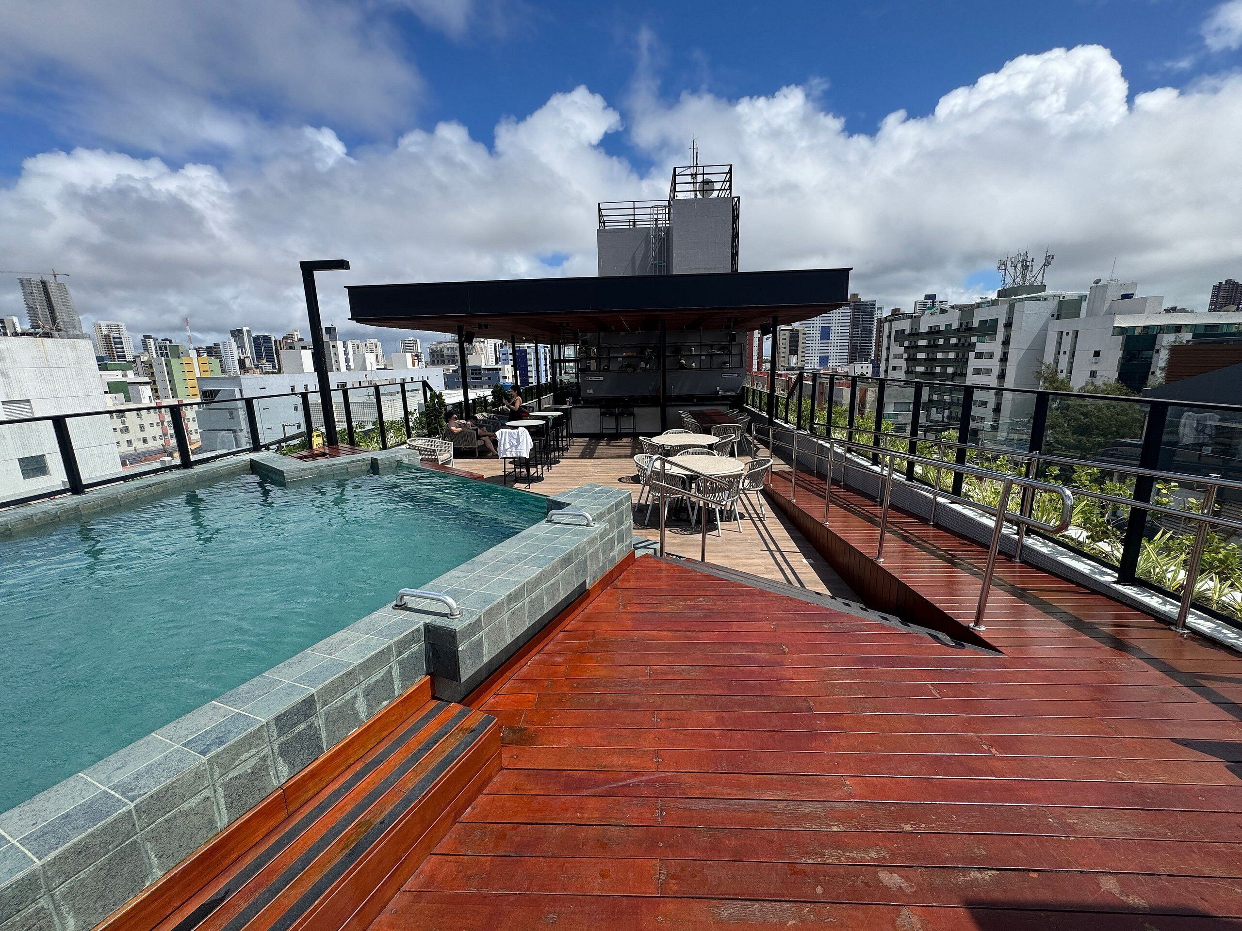Uma área de piscina no terraço com vista para o horizonte da cidade, mobiliário de exterior e um espaço de bar coberto.