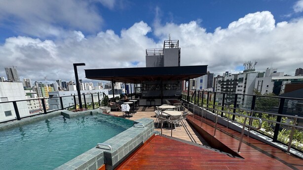 A rooftop pool area with a view of the city skyline, outdoor seating, and a covered bar area. - Breeze Studio Vista Mar Jardim Oceania (João Pessoa)