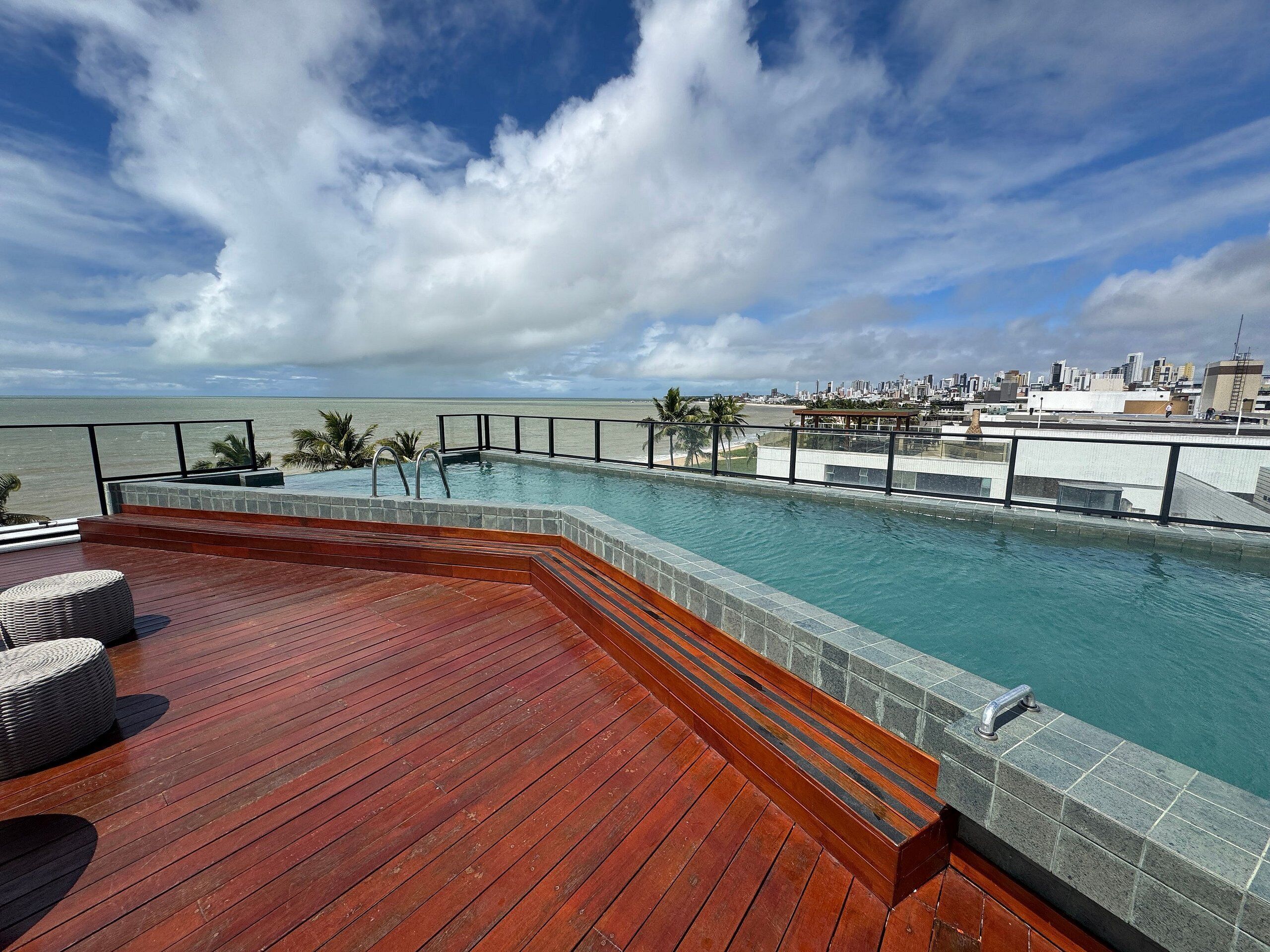 A rooftop infinity pool with a wooden deck and a cityscape view.