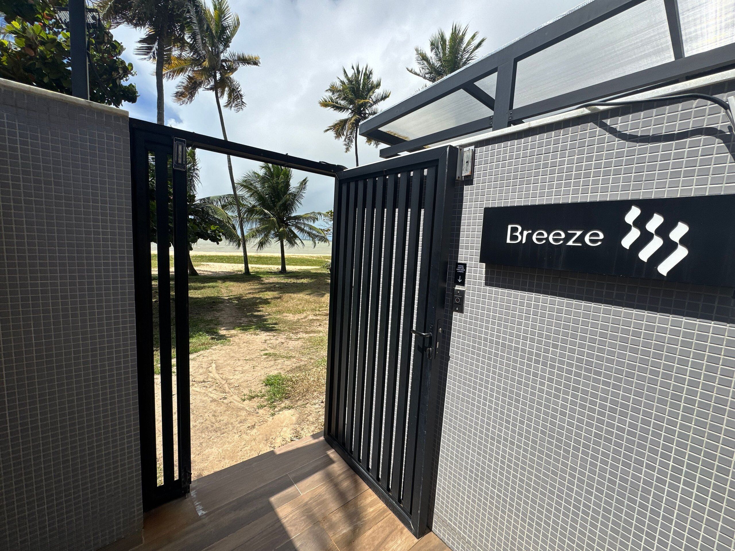 A gated entrance to a property named 'Breeze' with a view of a beach and palm trees.